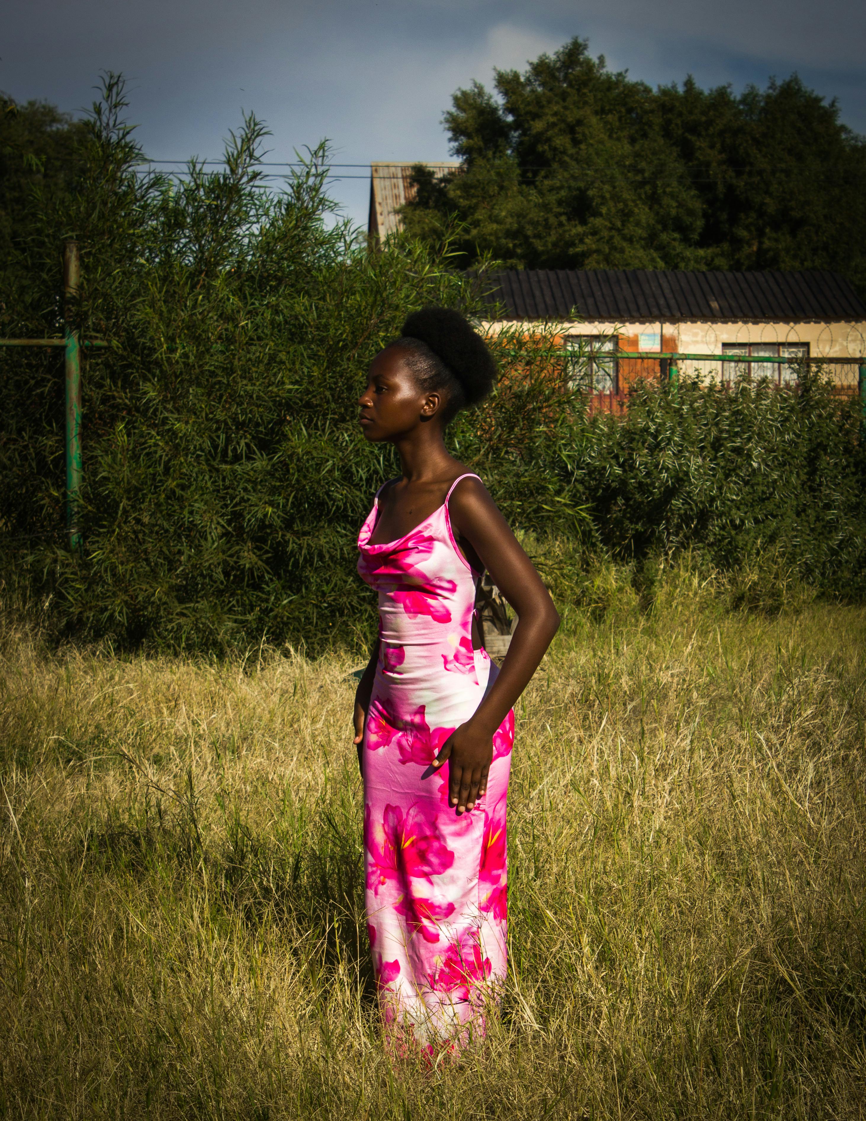 Portrait of a woman in a vibrant pink dress standing outdoors in a lush grassy field.