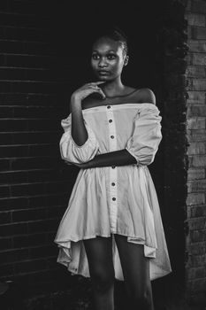 A striking black and white portrait of a young woman in elegant attire, standing confidently against a brick wall.