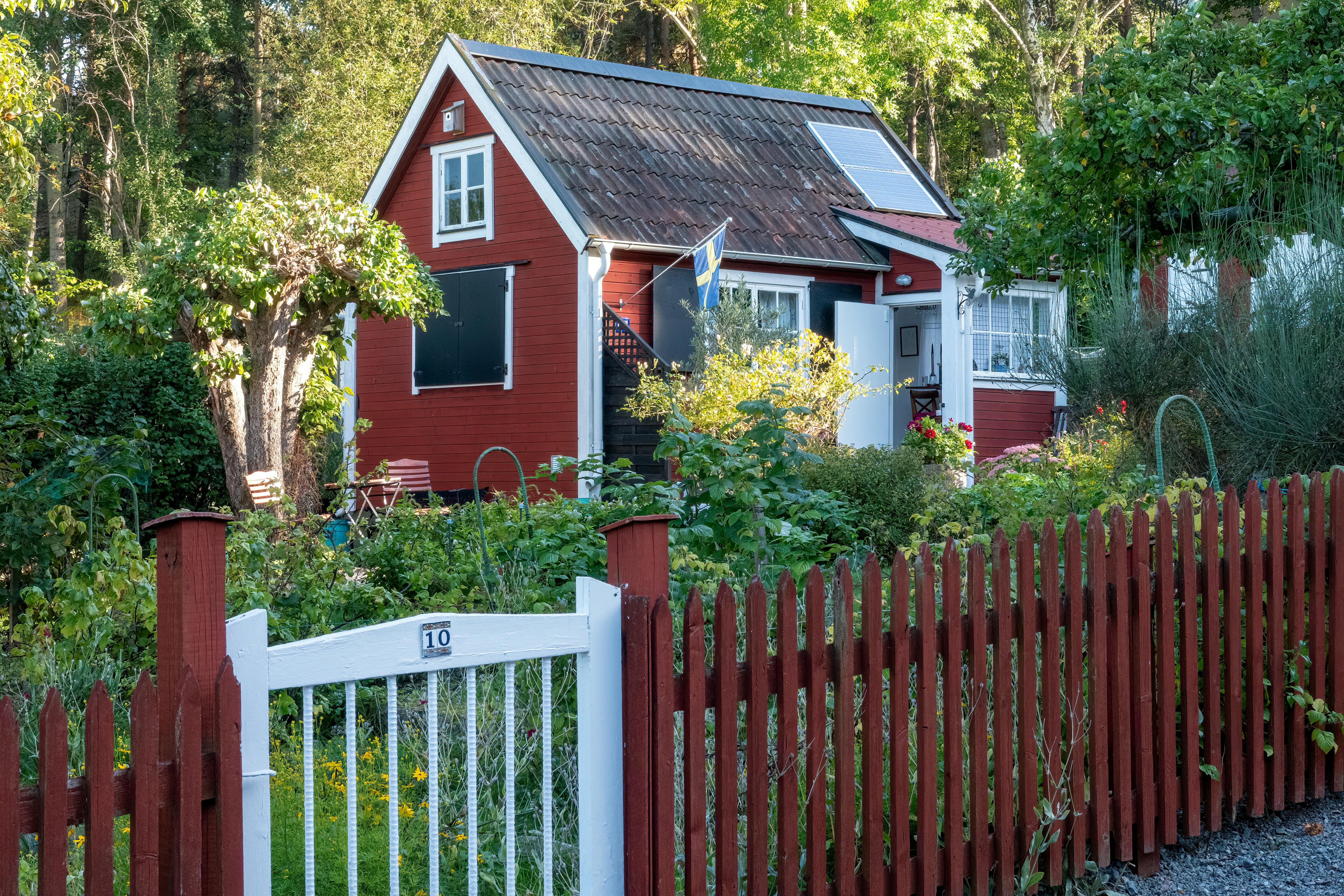 Picturesque red cottage with lush garden, solar panels, and Swedish flag in Stockholm.