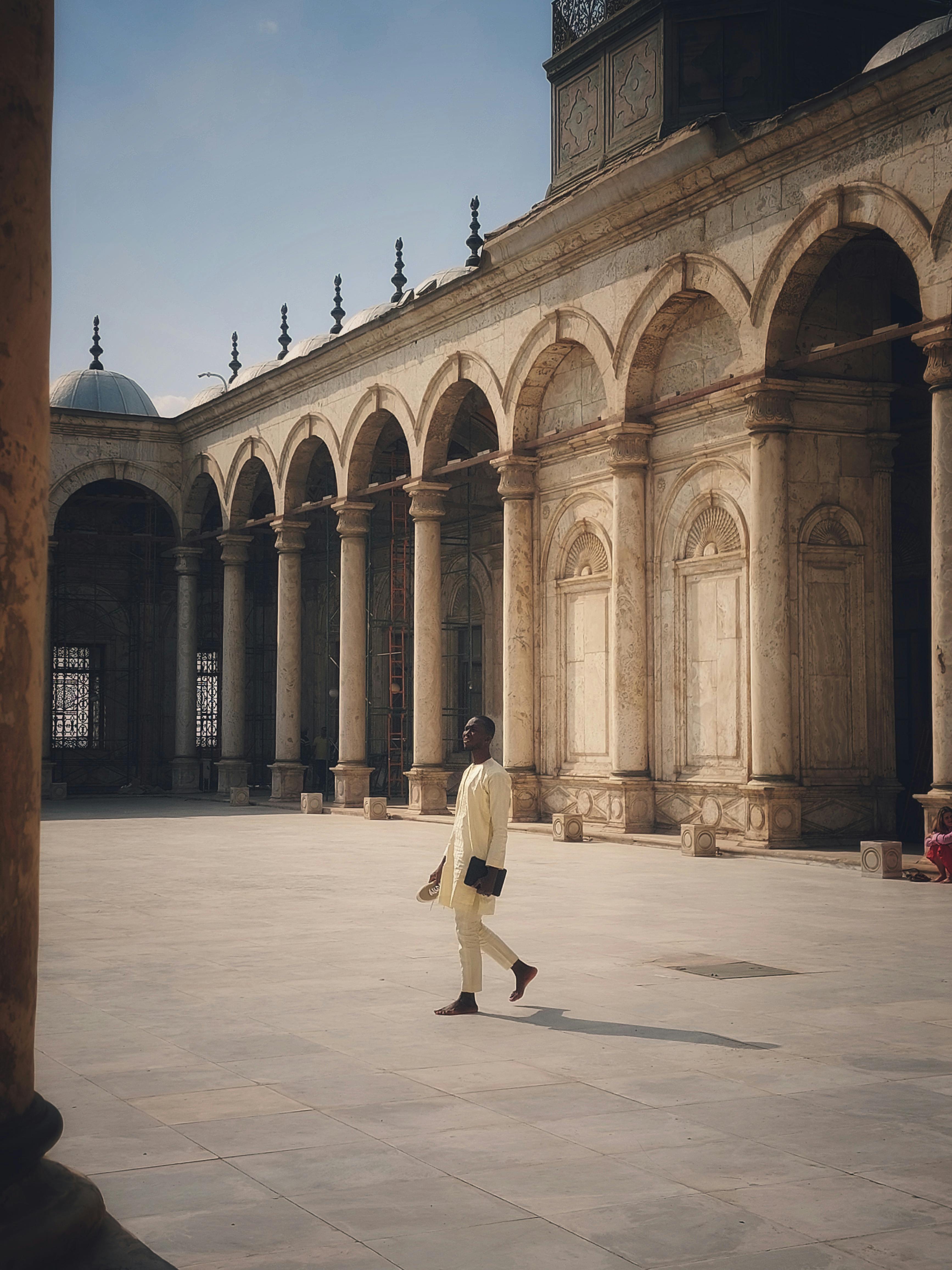 A man walks in the spacious courtyard of a historic mosque, showcasing stunning architecture.