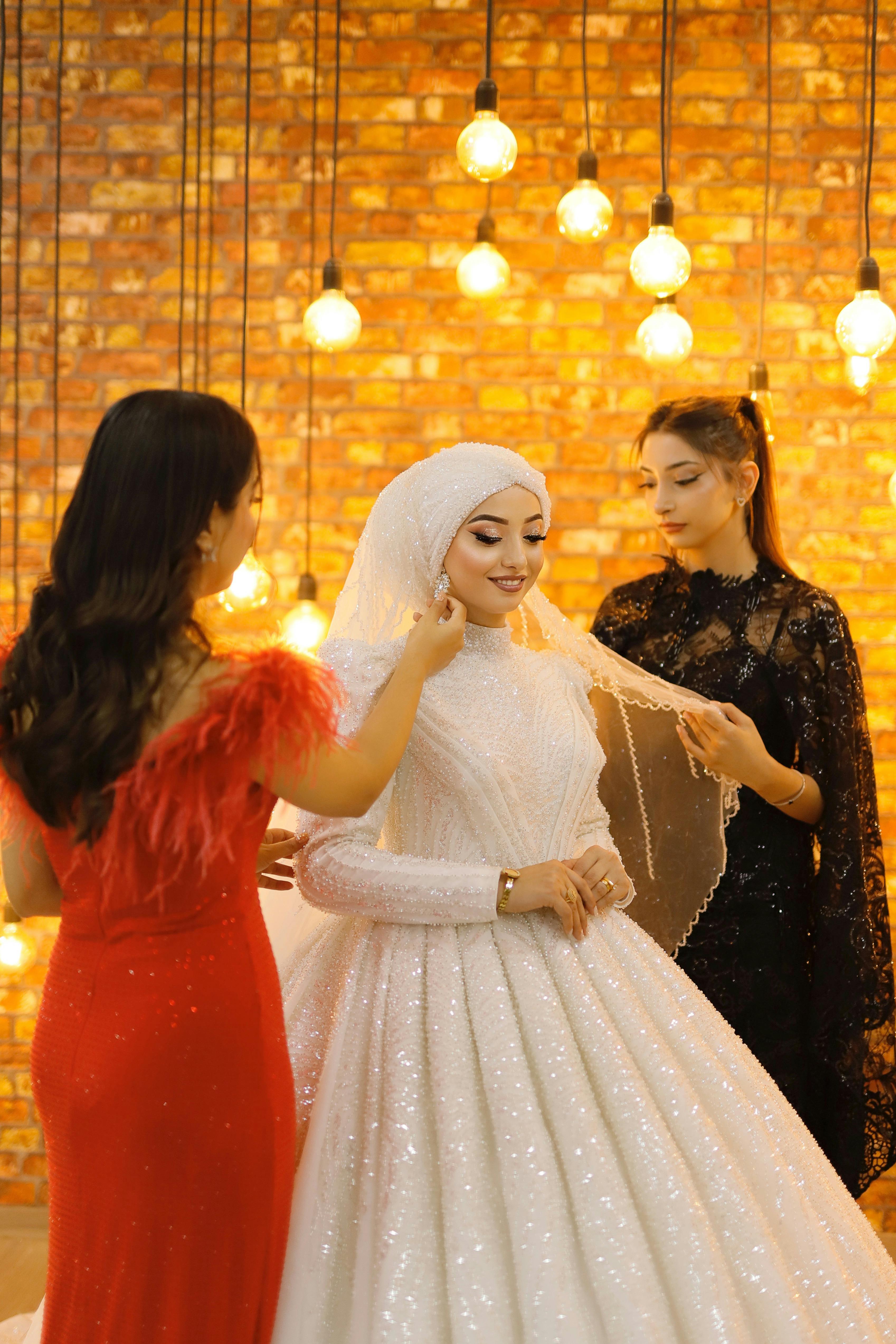 A bride in a shimmering gown with friends adjusting her veil.