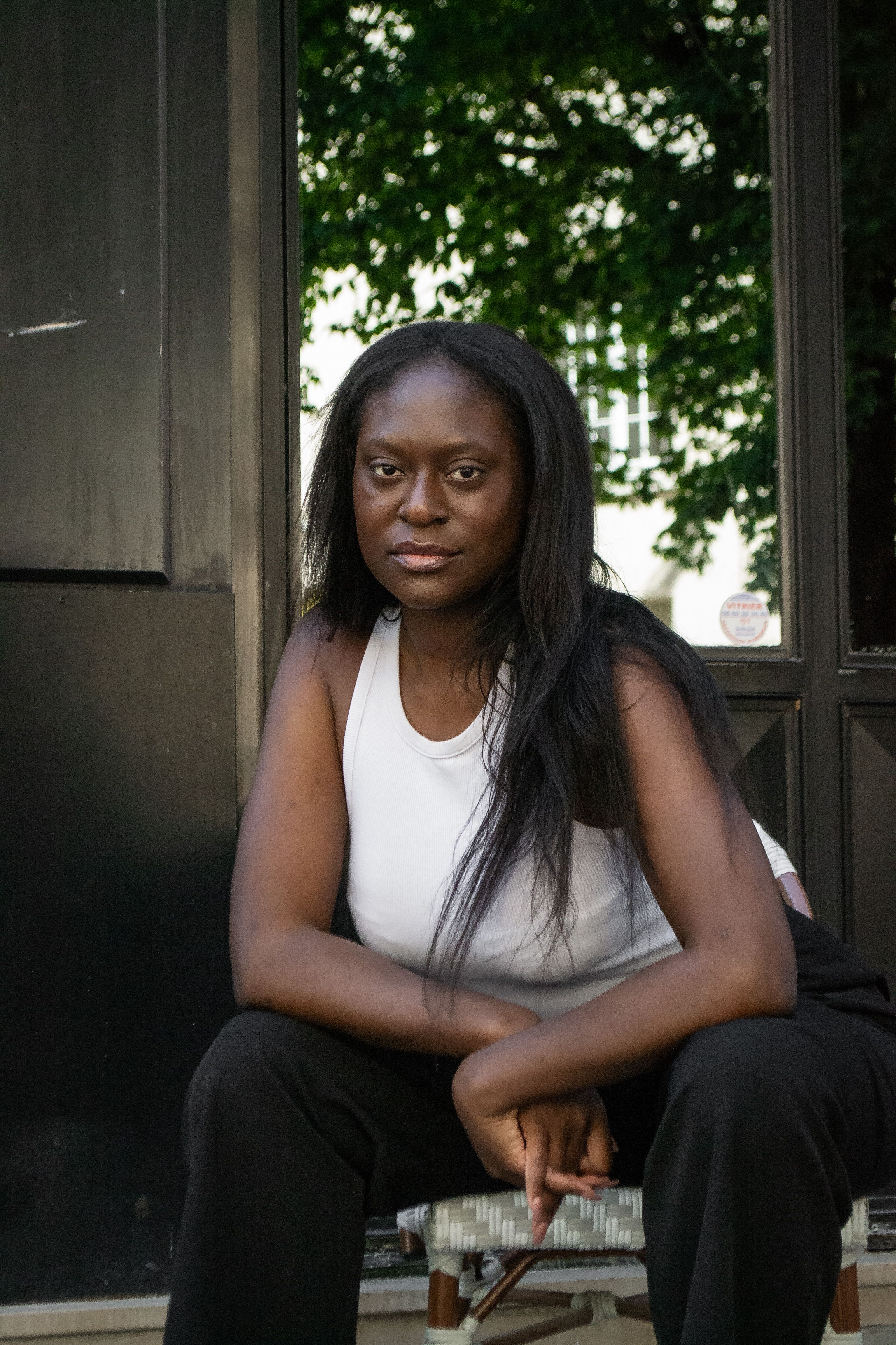 A confident black woman in casual attire sitting outdoors with a serene expression.
