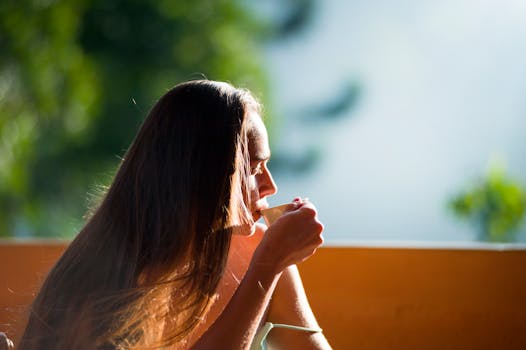 A woman peacefully sipping tea outdoors in the morning sunlight.