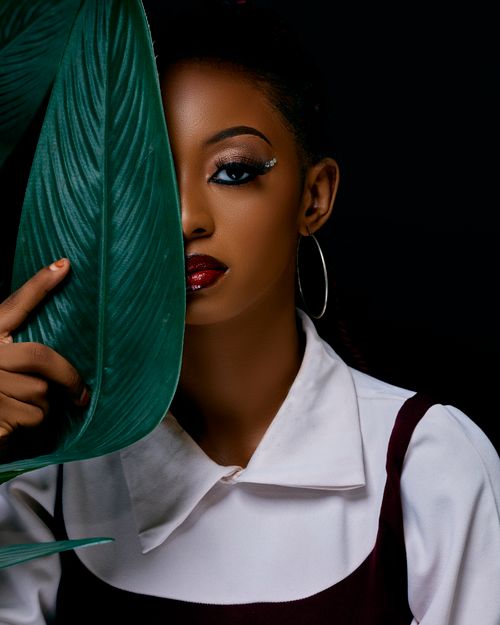 Free Elegant portrait of a woman half-concealed by a large green leaf, showcasing unique makeup and fashion. Stock Photo