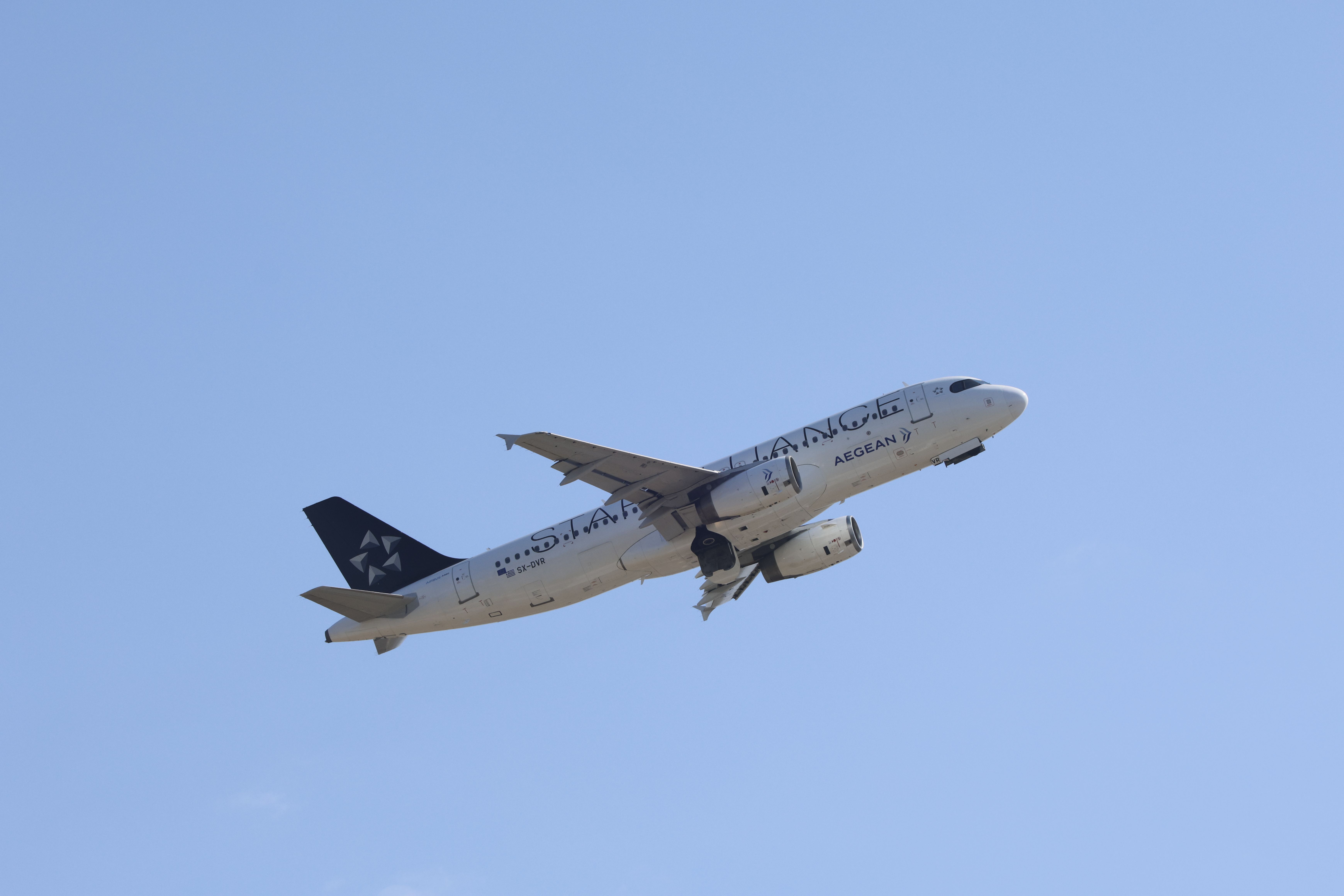 Aegean Airlines plane flying mid-air against a bright blue sky.