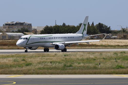 White and green commercial airplane taxiing on runway at a sunny airport.