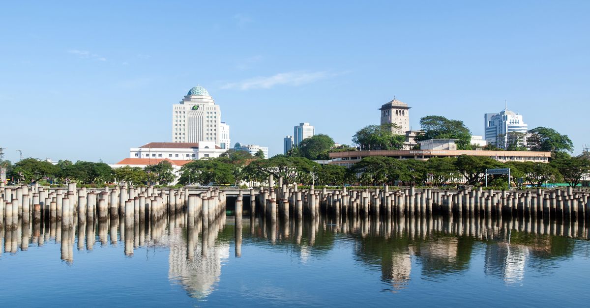 Beautiful view of Johor Bahru skyline reflecting on calm water on a sunny day.