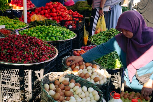 A bustling local market stall with vibrant vegetables and eggs, featuring a shopper in a hijab.