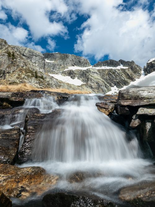 Free Stunning capture of a waterfall cascading over rocks in a mountainous landscape under a bright blue sky. Stock Photo