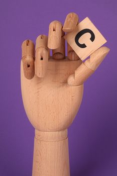 Wooden mannequin hand holds a letter block against a vibrant purple backdrop.