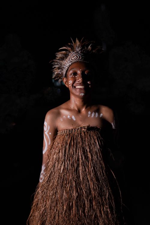 Free A smiling individual wearing traditional tribal clothing with face paint, captured at night. Stock Photo