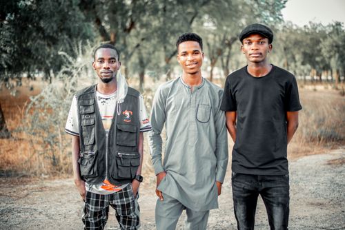 Free A group of three young men standing together outdoors, smiling warmly at the camera. Stock Photo