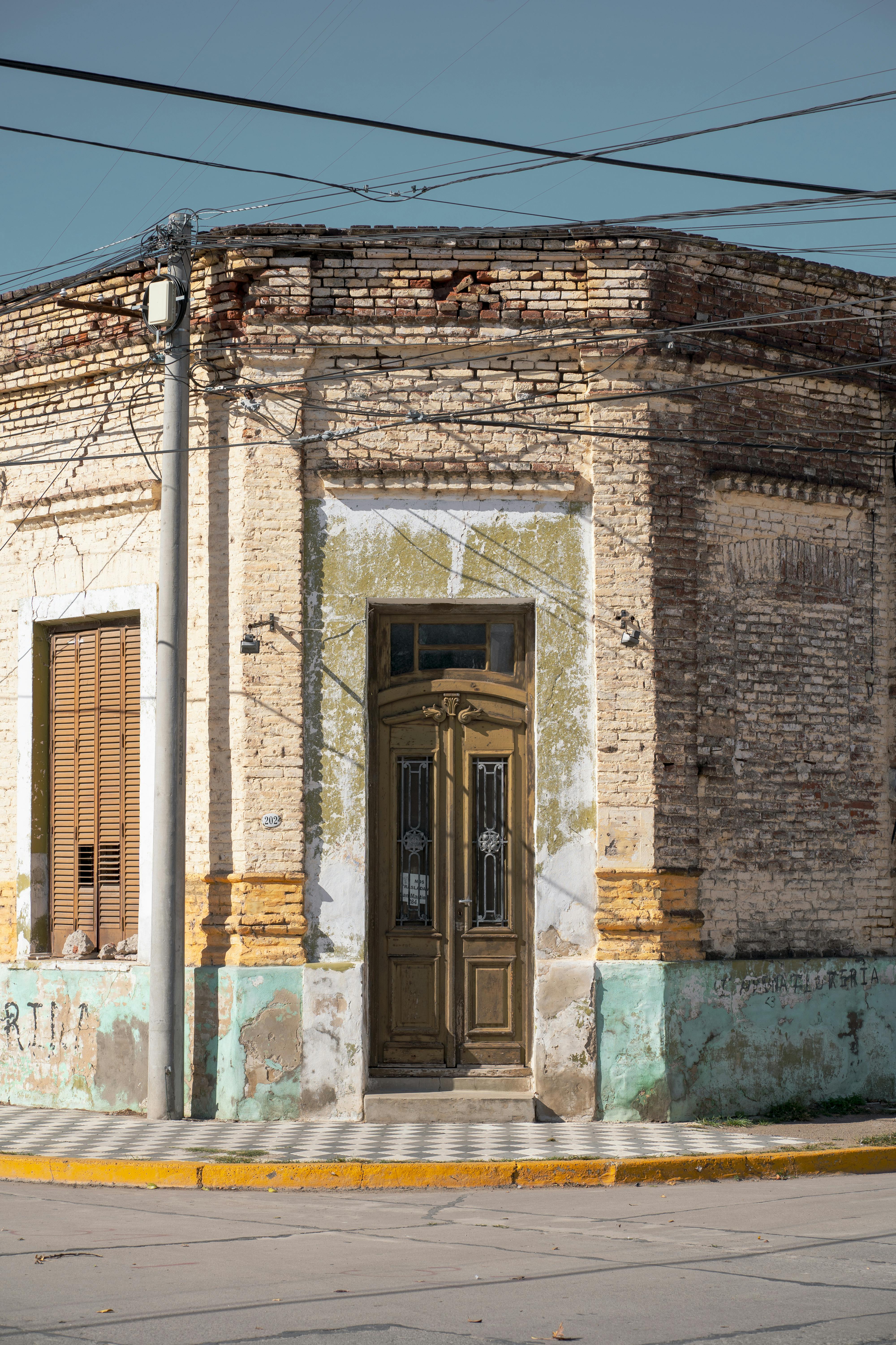 Free Historic corner building with weathered brick and wooden door in Oliva, Córdoba, Argentina. Stock Photo