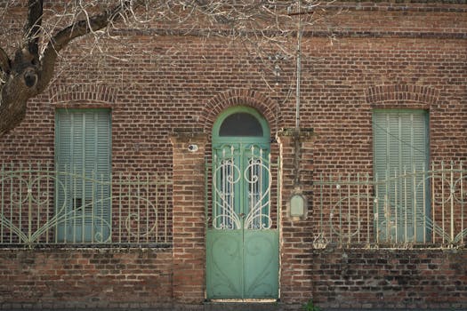 Charming brick building facade featuring turquoise shutters and wrought iron grille in Oliva, Córdoba, Argentina.