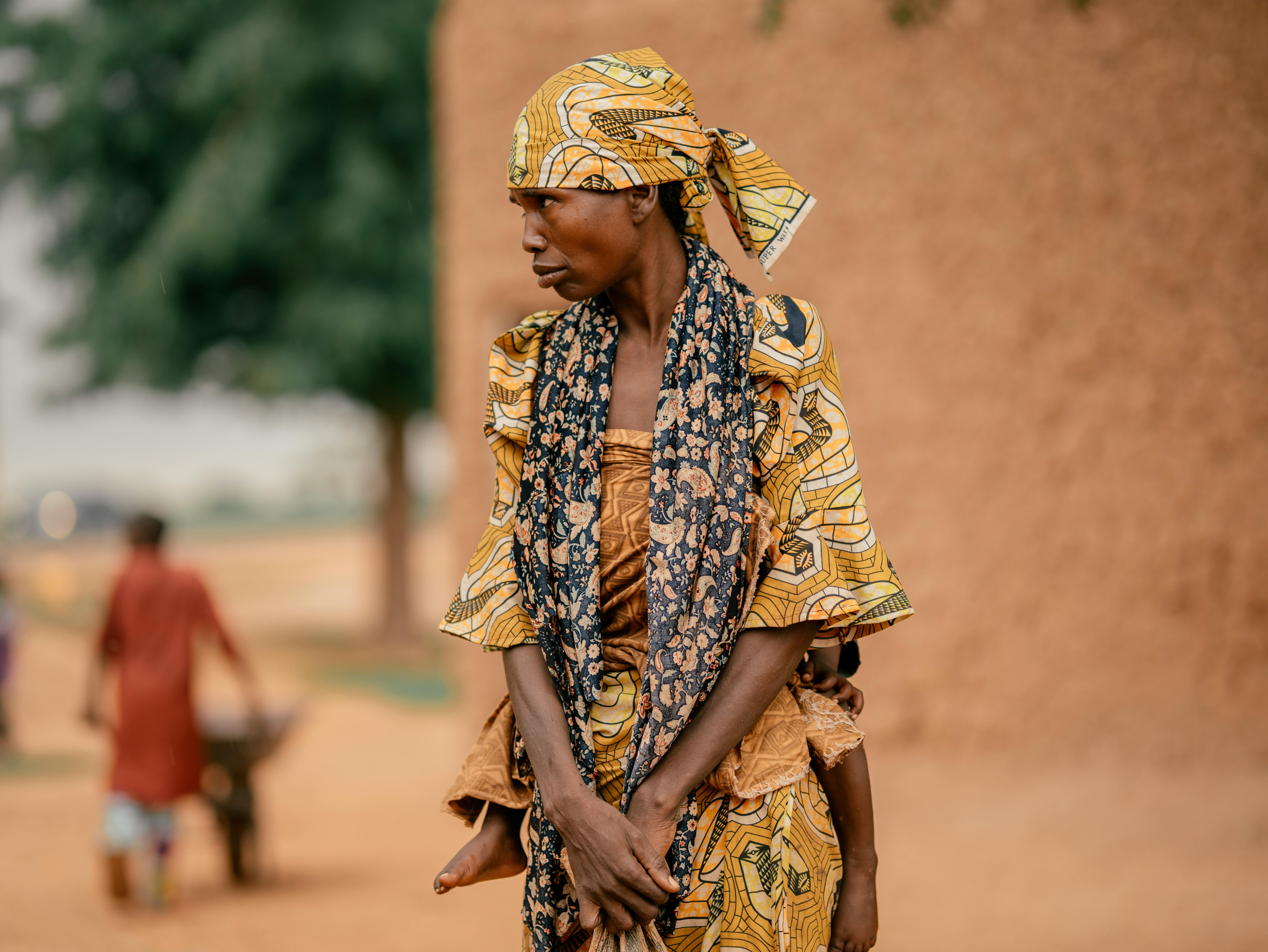 African woman in traditional clothing with child, standing outdoors in Nigeria.