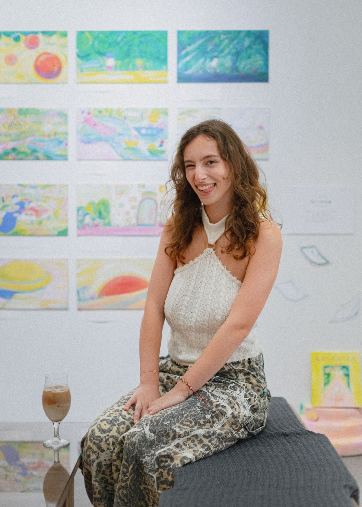 An artist seated in a gallery among small colourful works