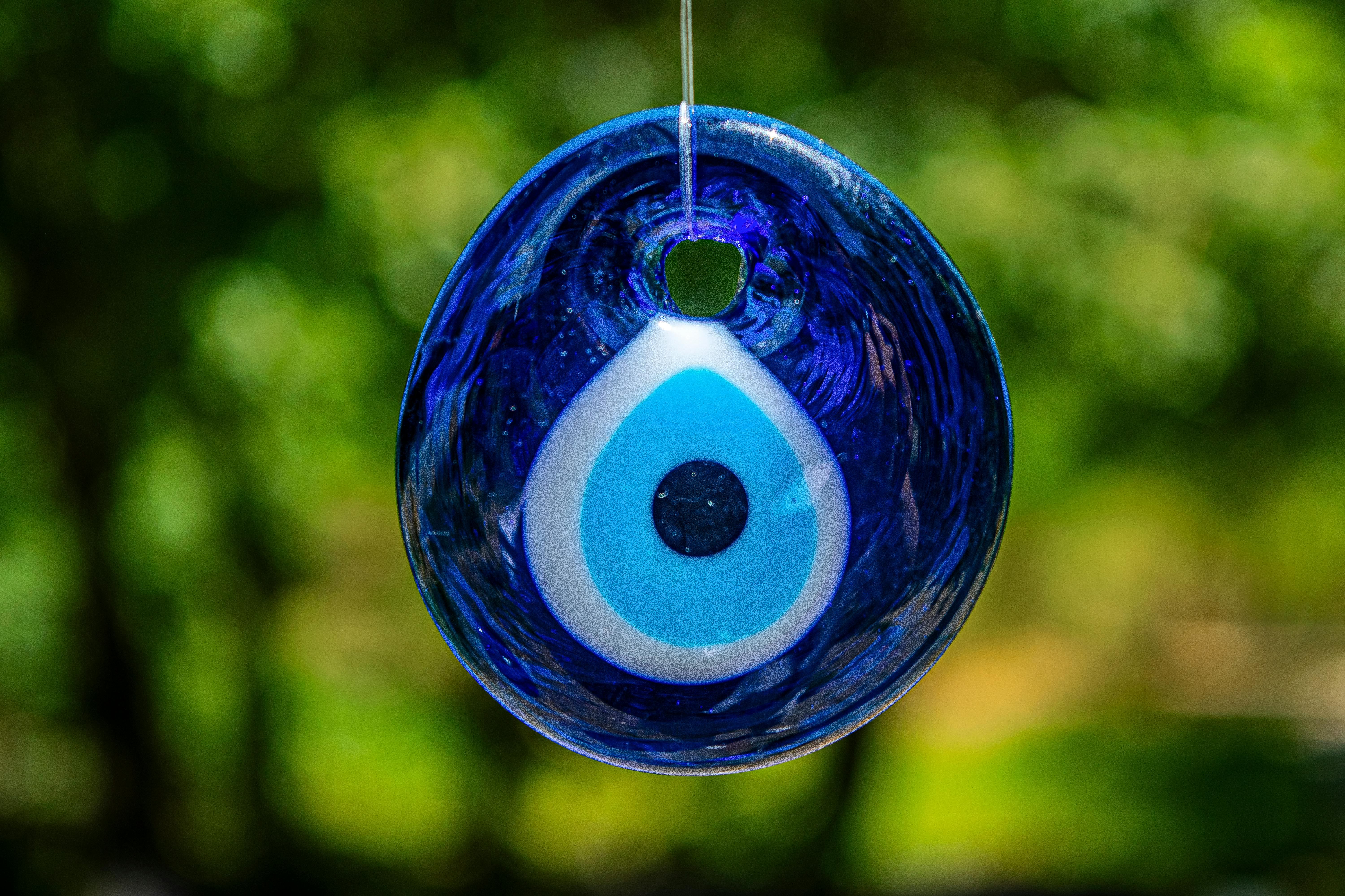 Close-up of a blue evil eye glass pendant hanging outdoors, symbolizing protection.