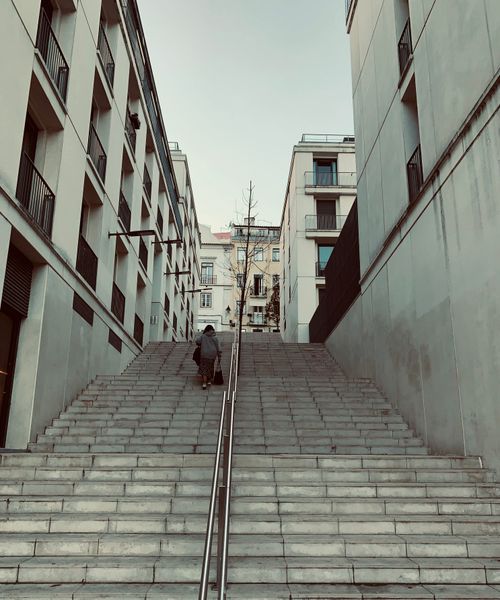 Free A person ascending a wide stone stairway between residential buildings in the city. Stock Photo