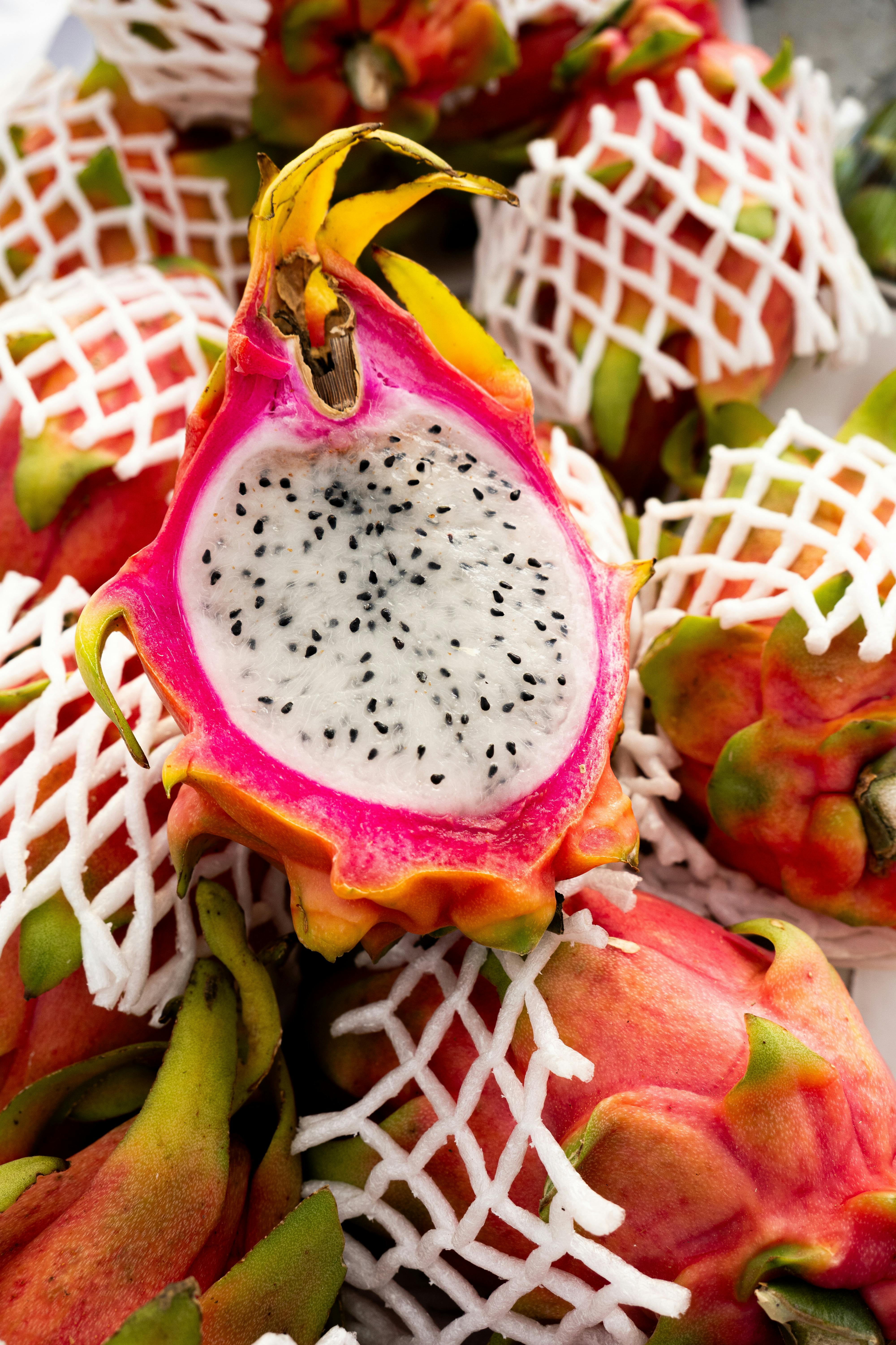 Close-up of sliced dragon fruit with netted fruit in background, highlighting tropical colors and textures.