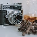 一台老式相机的特写镜头旁，干熏衣草点缀其间，白色表面映照着童话般的灯光