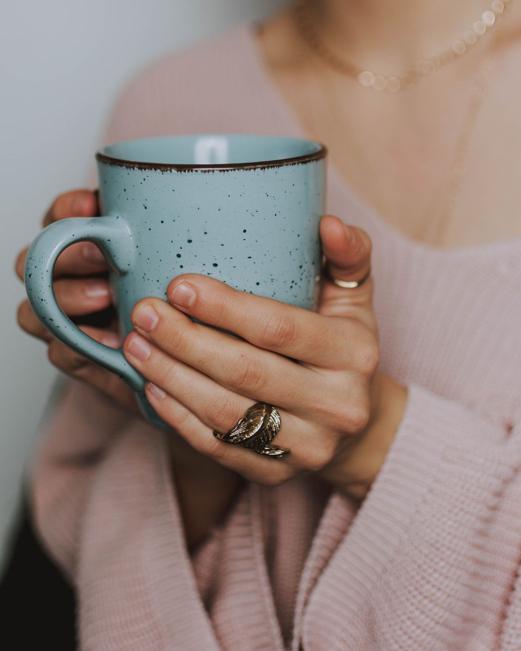 A close-up of a woman's hands holding a blue ceramic mug, wearing a cozy sweater.. close, womans, hands