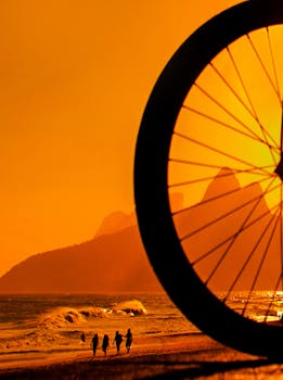 Silhouetted cyclists capture the scenic sunset at Ipanema Beach, Rio de Janeiro, with vibrant orange hues and iconic mountains in the background.