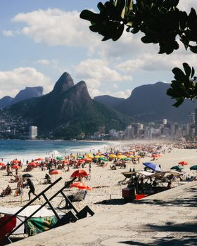 Crowded Ipanema Beach in Rio de Janeiro with vibrant umbrellas and Two Brothers Mountain view.