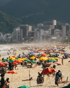 Colorful umbrellas and busy crowds on Ipanema beach, Rio de Janeiro, with city skyline.