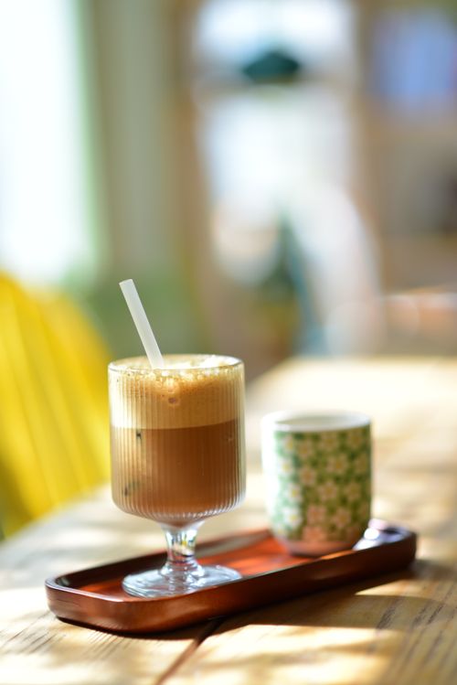 Free Glass of iced coffee and patterned cup on wooden table with sunlight, offering a cozy vibe. Stock Photo