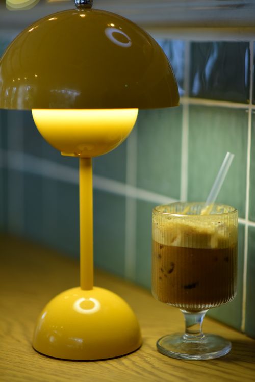 Free A retro yellow lamp illuminates an iced coffee on a wooden table, creating a cozy ambiance. Stock Photo