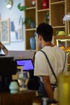 A barista in a coffee shop assisting a customer, with a casual and modern interior setting.
