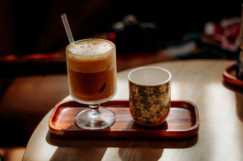 Free A warm ambience showcasing a frothy iced coffee and floral mug on a wooden tray. Stock Photo