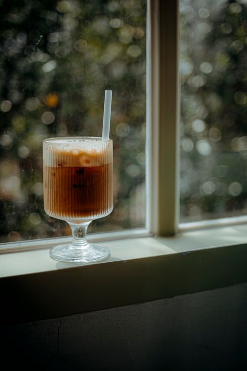 Free A refreshing iced coffee in a glass with straw placed on a window sill with sunlight. Stock Photo