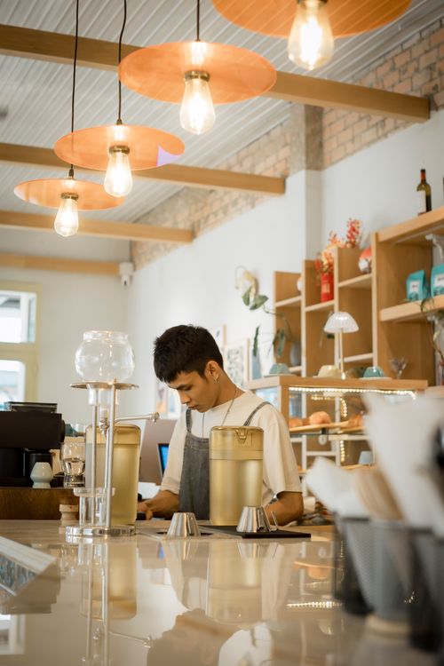 Free Barista in modern cafe with warm lighting and decor, preparing drinks. Stock Photo