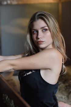 Elegant indoor portrait of a woman with long blonde hair wearing a black slip dress, looking contemplative.