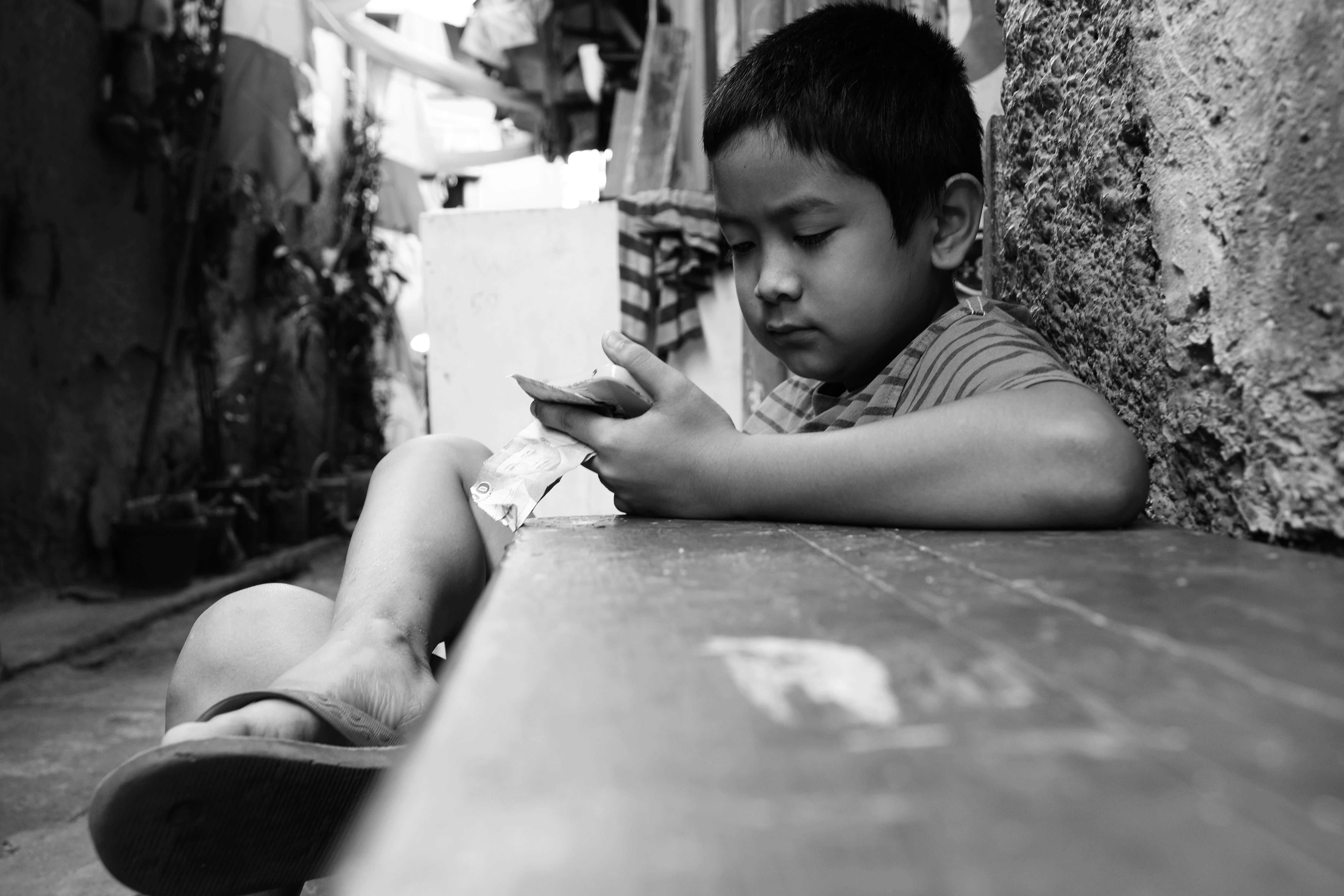 A young boy reads intently while sitting in an alley in Jawa Barat, Indonesia.