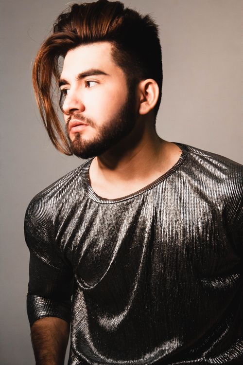 Free A fashionable young man with a beard poses in a metallic top, exuding confidence and modern style. Stock Photo
