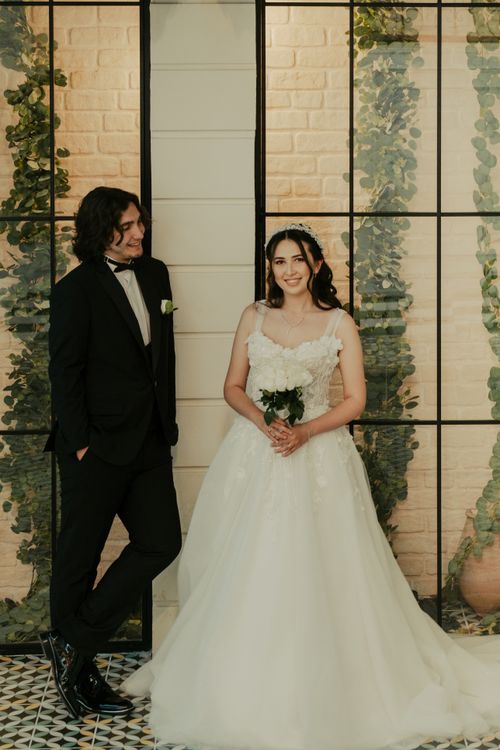 Free A beautiful indoor wedding portrait featuring a smiling bride and groom in elegant attire. Stock Photo