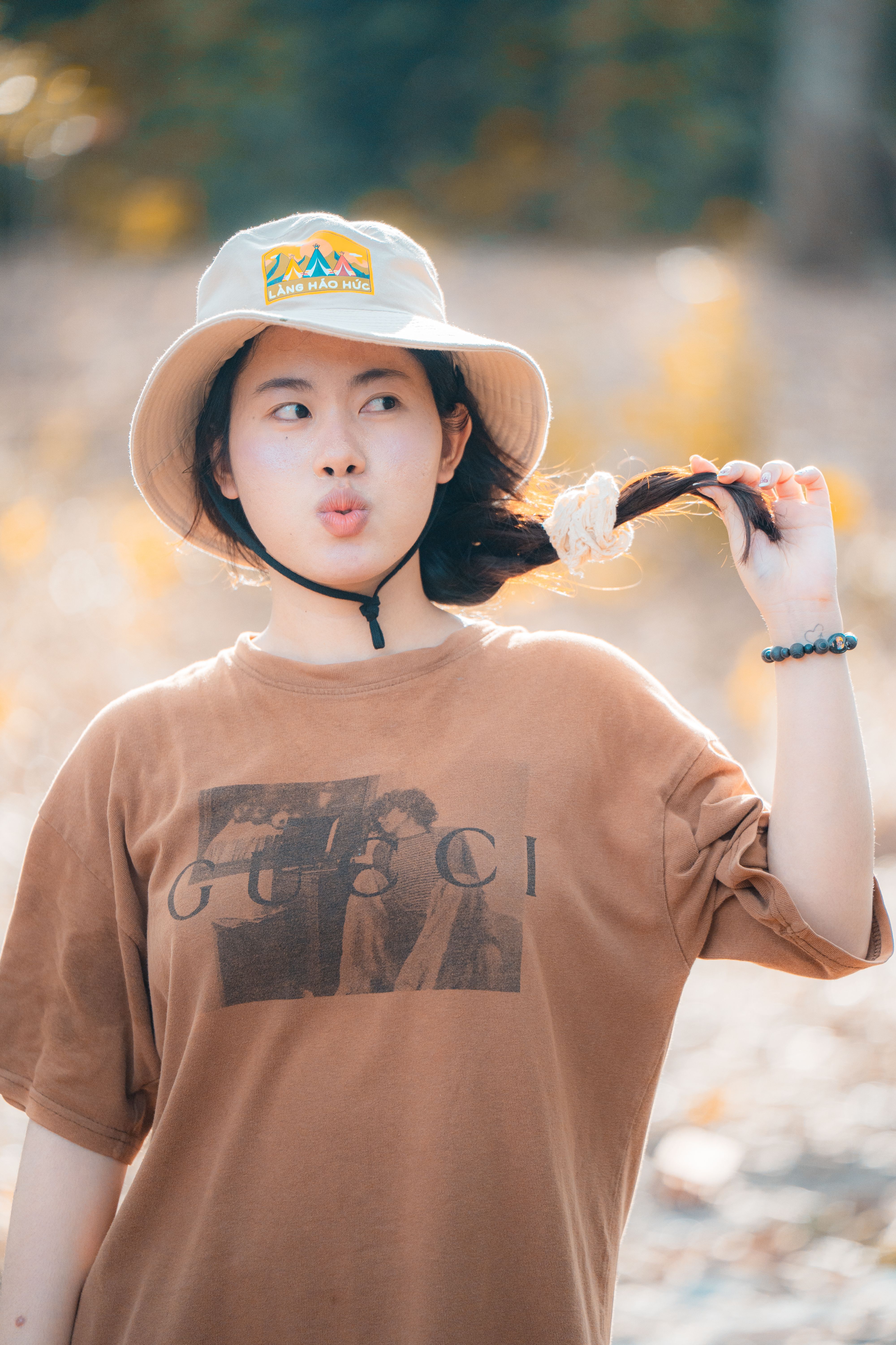 A young woman in a hat enjoys a sunny day outdoors, playfully pulling her hair.