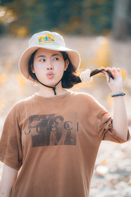 A young woman in a hat enjoys a sunny day outdoors, playfully pulling her hair.