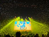 音乐会现场充满活力，灯光闪烁，五彩纸屑飞扬，人群正欣赏着精彩的表演