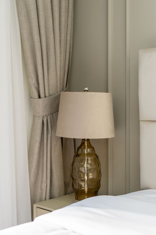 Free A serene bedroom corner featuring a chic lamp and beige decor in Dubai. Stock Photo