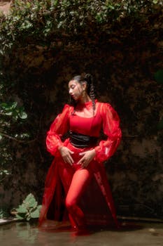 Dramatic fashion portrait of a woman in a red dress posing elegantly by water outdoors.