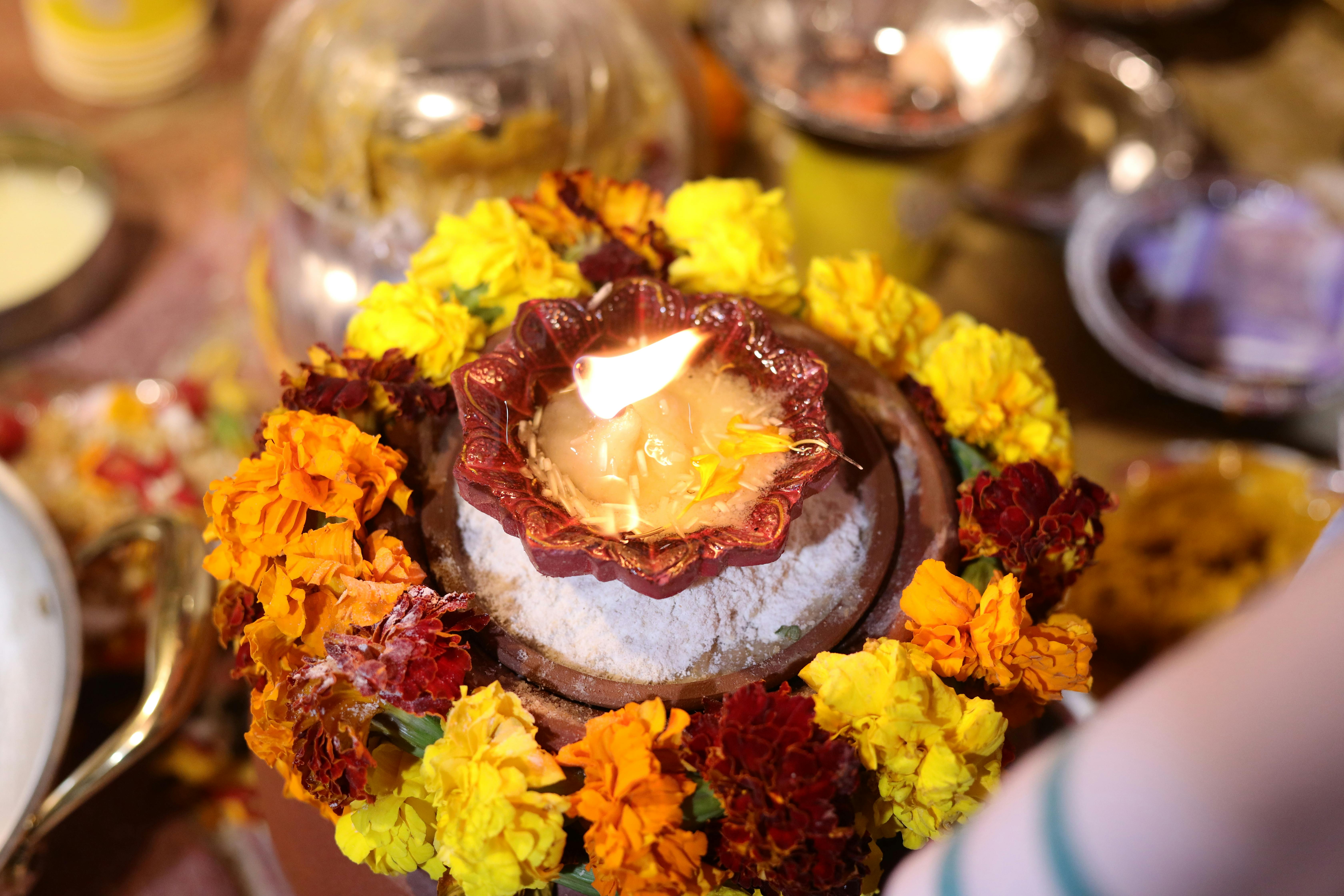 A vibrant display of marigold flowers surrounding a lit ghee lamp used in a traditional Indian ceremonial setup.