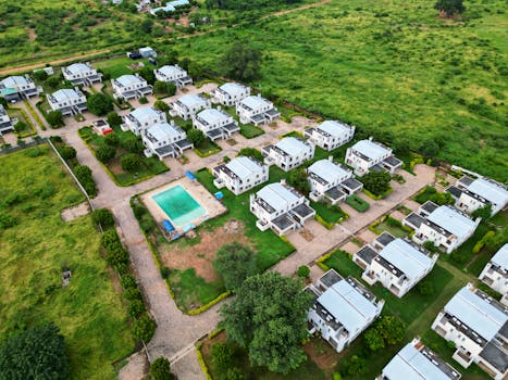 Aerial photograph of a modern housing estate with a communal pool, surrounded by lush greenery.