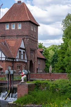 Historic brick tower by the riverside with lush greenery and statuesque art in a summer setting.
