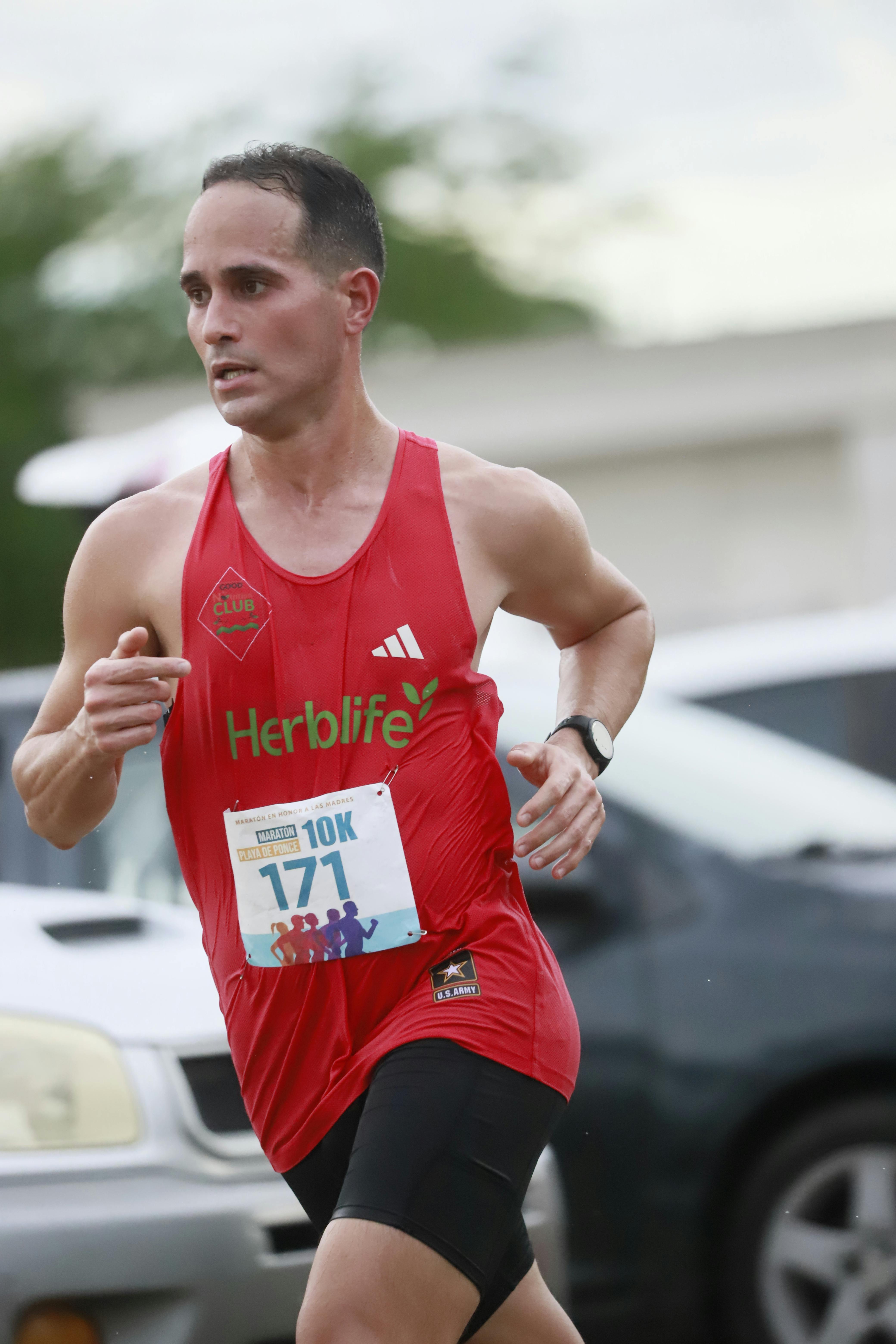 Male athlete in red tank top running a 10K marathon outdoors.