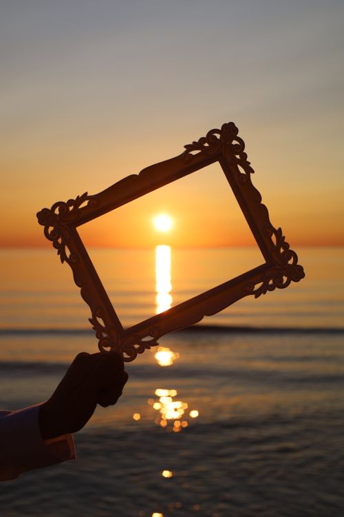 Free A decorative frame held against a stunning ocean sunset, capturing the golden hour glow. Stock Photo
