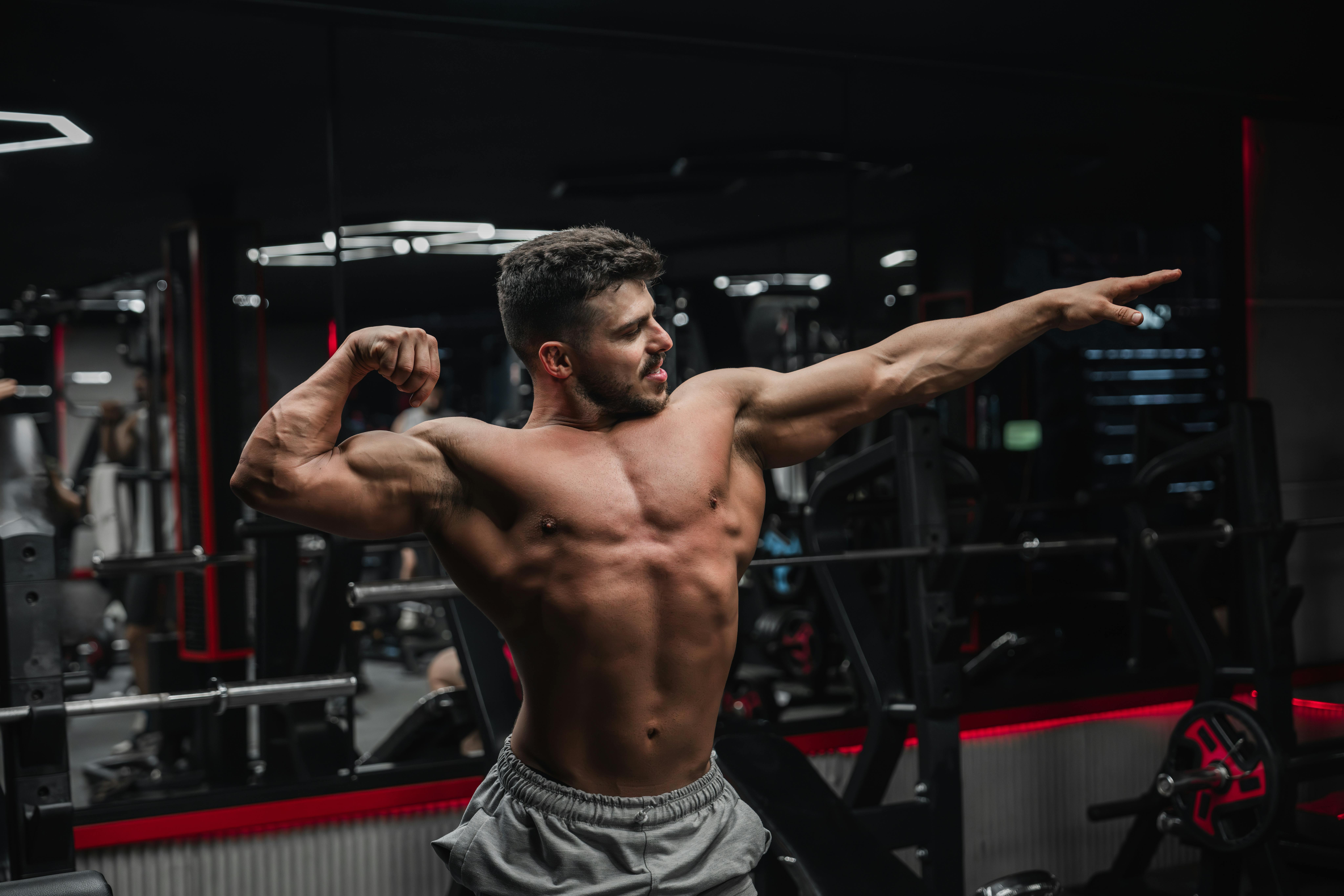 Strong shirtless man flexing muscles in a gym, showcasing fitness and determination.