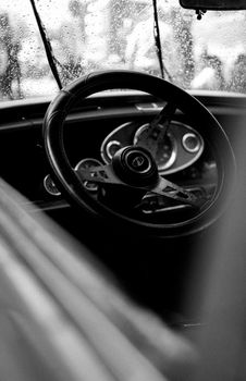 Black and white photo of a vintage car interior with a steering wheel, taken in rainy Napoli, Italy.